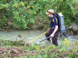 WVU student walking in stream with backpack and poles
